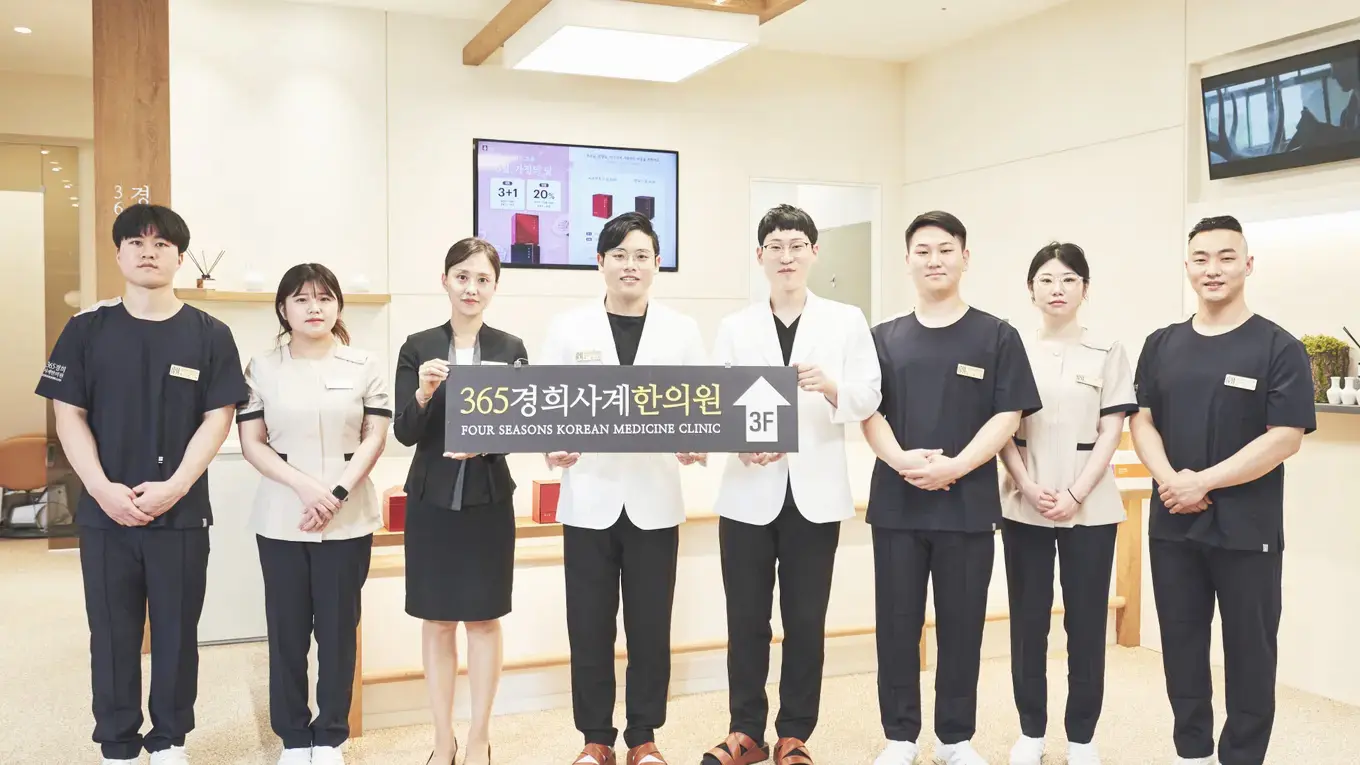 365경희사계한의원 구성원이 대기 공간에서 한의원 이름이 적힌 안내판을 들고 서 있는 모습