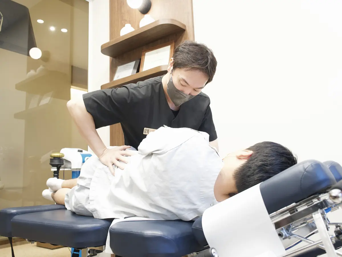 한의사가 치료 침대에 누운 환자의 허리에 손을 얹고 추나 치료를 하는 모습