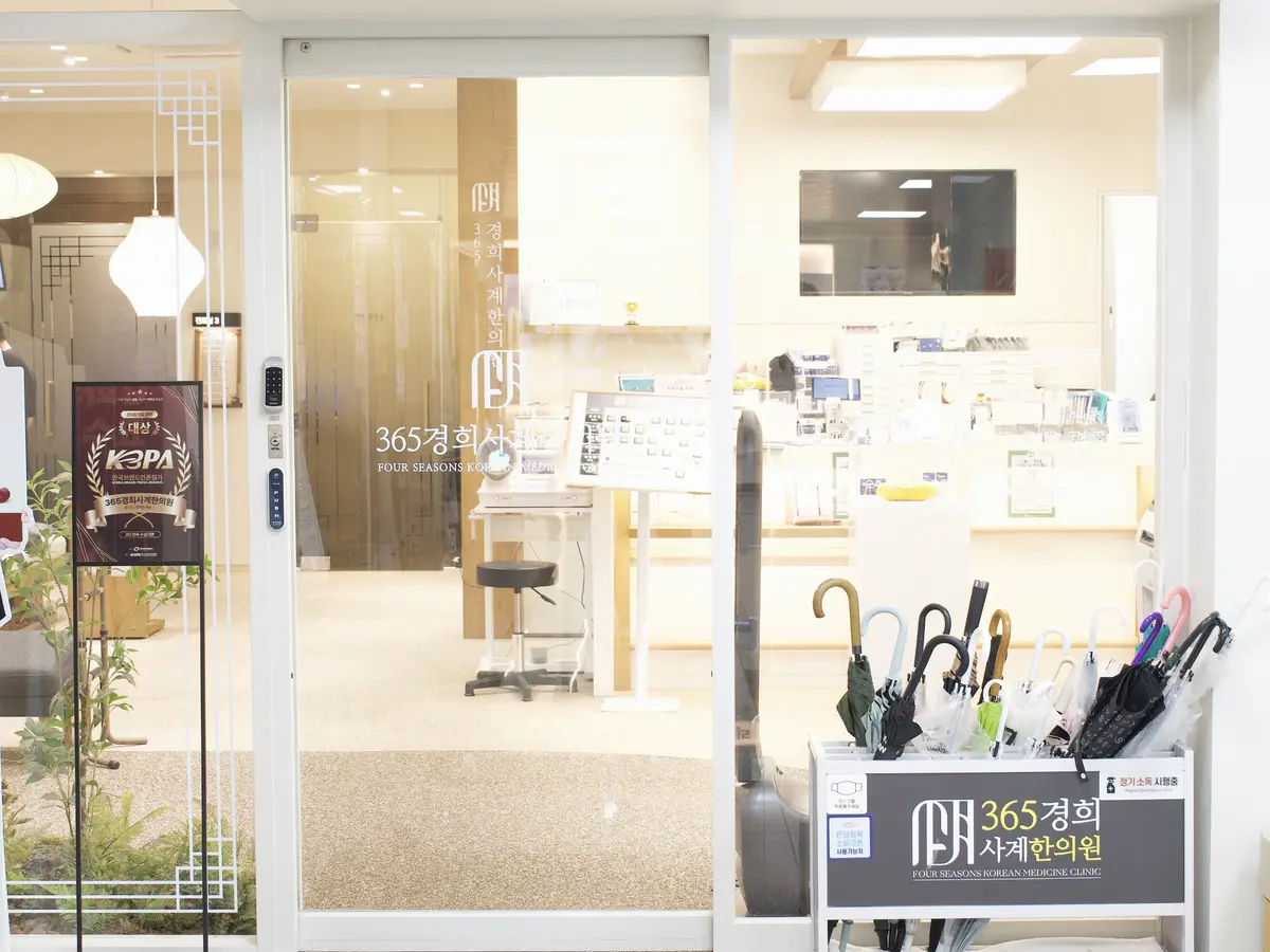 유리문 안쪽으로 접수 공간이 보이는 한의원 외래 출입구와 우산 꽂이